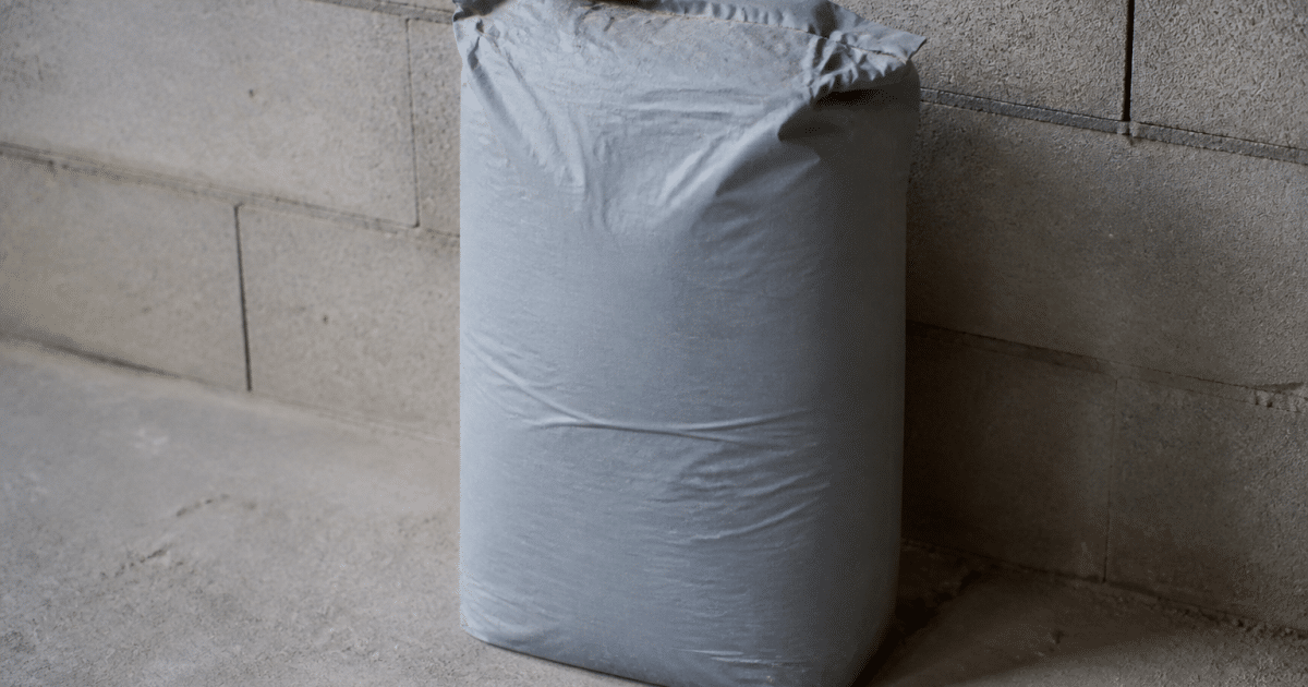 Sac gris mortier vingt-cinq kilos posé verticalement sur sol