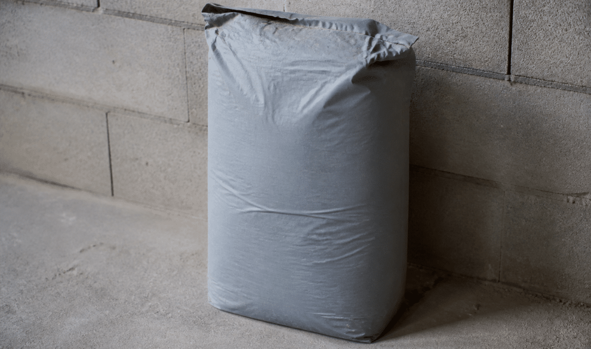 Sac gris mortier vingt-cinq kilos posé verticalement sur sol