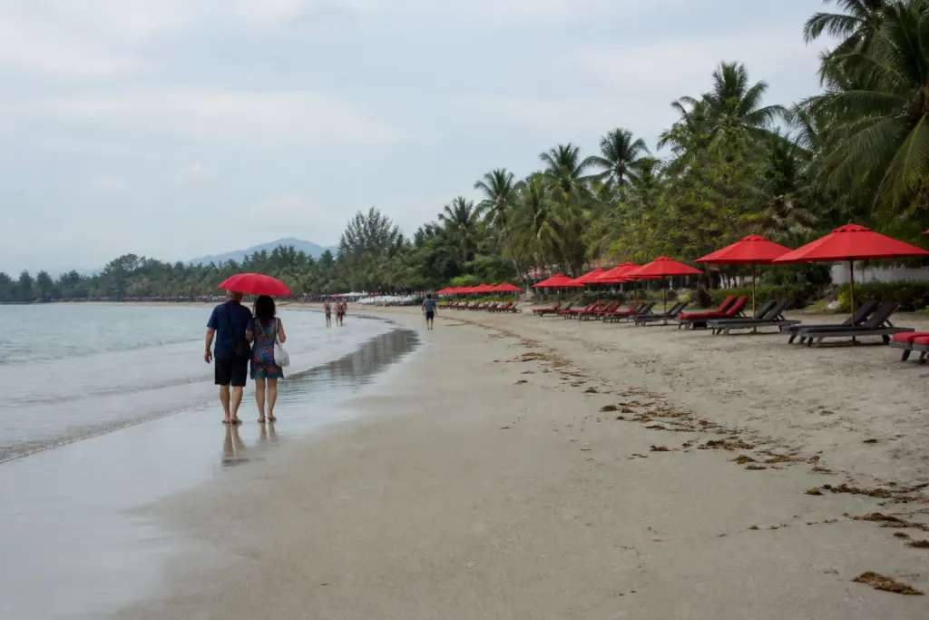Promeneurs sur la plage avec parasols rouges et palmiers